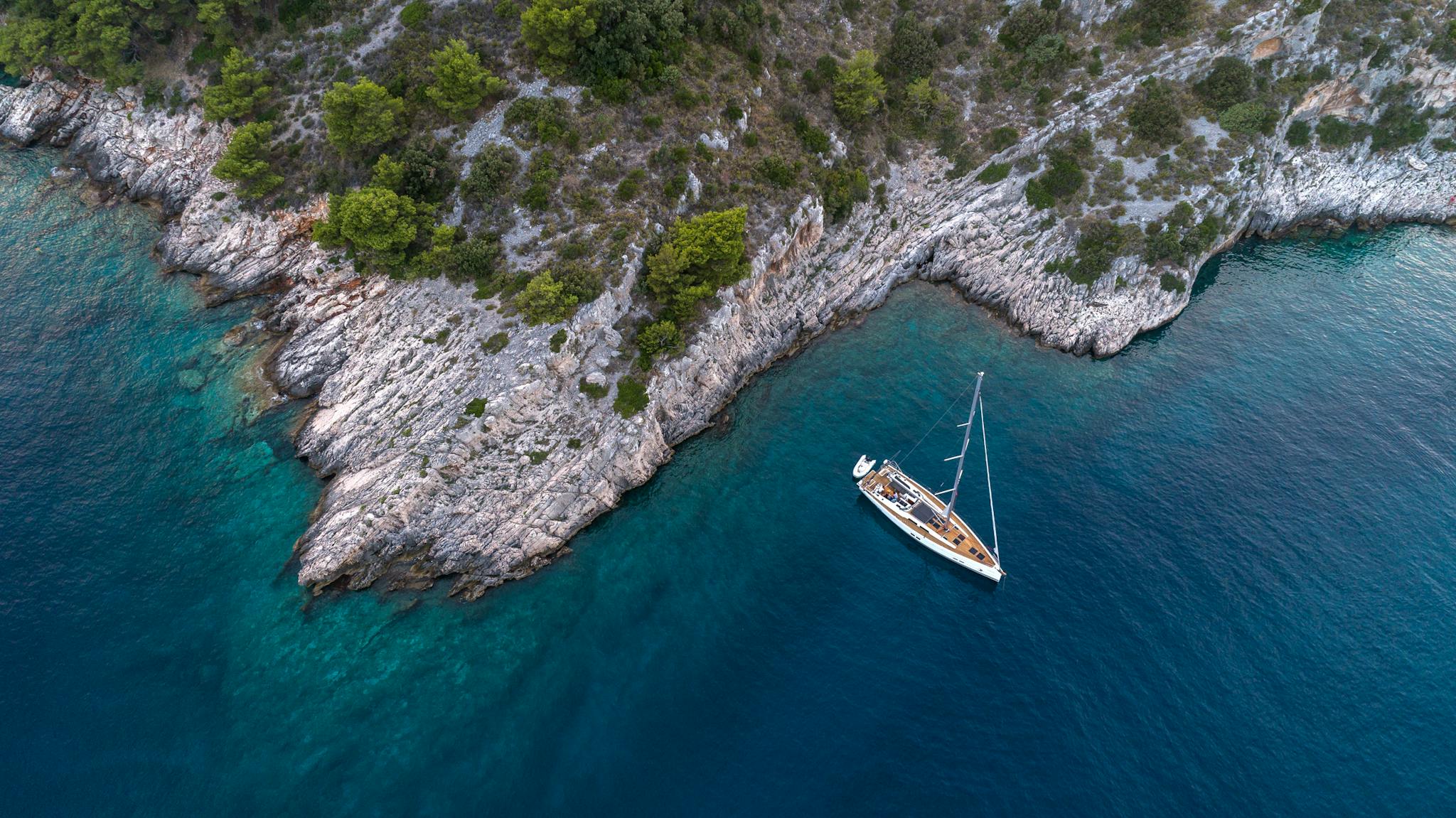 Aerial view of a sailboat sailing in a calm bay, with mountains in the distance.
